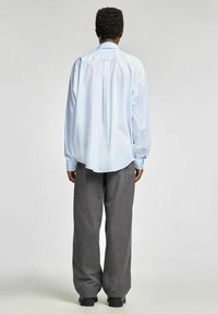 Jasnoniebieska koszula w paski z długim rękawem i zaokrąglonym dołem, zestawiona z szarymi spodniami w szerokie nogawki w drobną prążek oraz czarnymi butami.