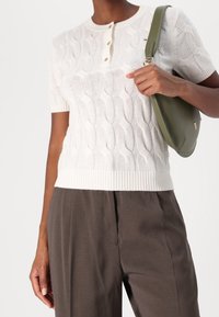 Pull blanc à manches courtes avec un motif en maille torsadée texturée, doté d'un col rond et d'une patte de boutonnage à trois boutons. Assorti à un pantalon foncé.