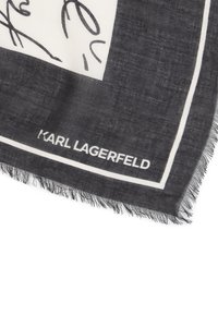 Schwarz-weißes Schal mit fringiertem Rand, das ein strukturiertes Muster aufweist und ein signiertes "KARL LAGERFELD"-Etikett in fetten weißen Buchstaben trägt.