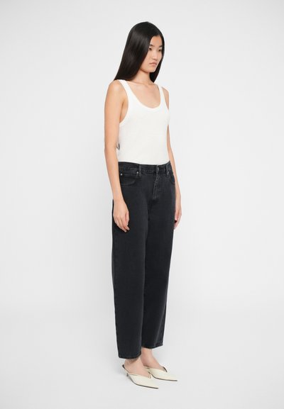 Svarte jeans i denim med rett benpassform, høy midje og lommer foran; kombinert med et tettsittende hvitt tanktopp og beige spisse sko.