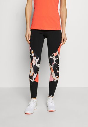 Svarta leggings med abstrakta orange och crème accentpaneler, tillsammans med en korallfärgad åtsittande topp och vita löparskor.