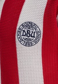 Rød- og hvidstribet strikstof med en cirkulær DSU-logo-patch broderet med sort tråd.