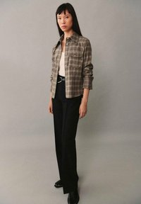 Ruutupaitainen ruskea napitettava paita, jossa on kaksi rintataskua, yhdistetty mustiin housuihin ja mustiin kenkiin. Sileä pinta, moderni siluetti.