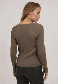 Rippiger brauner Pullover mit langen Ärmeln, einem weiten Ausschnitt und einem taillierten Saum. Das Material scheint weich mit einer strukturierten Oberfläche zu sein.
