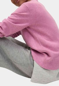 Maglione a maglia rosa con polsini e orlo a coste, indossato sopra pantaloni corti grigi melange. Il materiale sembra morbido e leggermente strutturato.