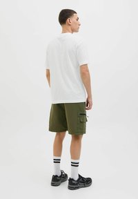 White cotton t-shirt and olive green cargo shorts with side pockets. Black athletic shoes and striped socks visible. Simple design overall.