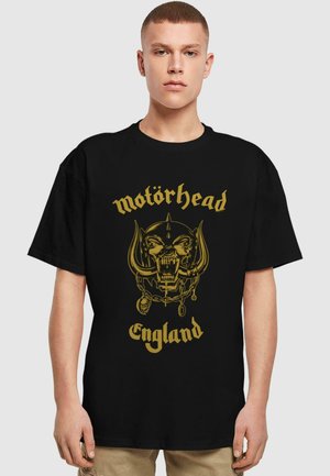 Sort bomulds T-shirt med en guld grafiktryk af et kranium med horn og kæder, mærket "Motörhead England" i bunden.