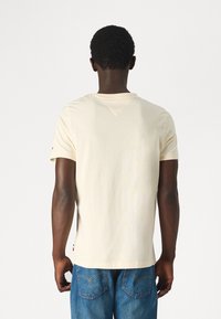 T-shirt di cotone color crema con maniche corte, scollatura arrotondata e un piccolo dettaglio con logo sulla manica; abbinato a jeans in denim blu.