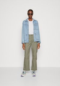 Light blue denim jacket, white t-shirt, olive green cargo pants, and multicolored sneakers. Accessories include black sunglasses and earrings.