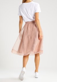 Ljusrosa, knälång kjol med ett genomskinligt överdrag, rynkad midja och en svävande design. Matchad med en vit t-shirt och sneakers.