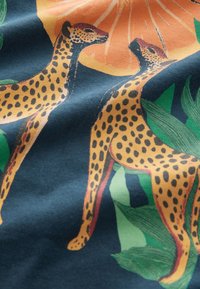 Värvikas kangas, millel on kaks kollasega mustade laikudega gepardi tumeda tausta taustal, ümbritsetud roheliste lehtede ja apelsiniviiluga.