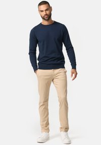 Svetrom modrý crewneck svetr vyrobený z bavlny, spárovaný se světlými béžovými chinos kalhotami a bílými teniskami, s uvolněným střihem a žebrovanými manžetami.