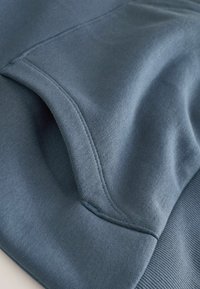 Ciemnoniebieska bluza wykonana z tkaniny o gładkiej teksturze, z kieszenią i ściągaczem u dołu, wyróżniająca się subtelnymi detalami szycia.