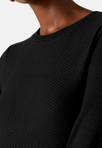 Pull en maille côtelée noir avec un col rond et un tissu texturé, mettant en avant des lignes verticales et des détails de manches ajustées.