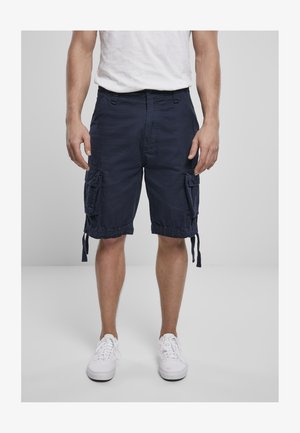 Mörkblå cargoshorts med dragsko i nederkant och flera sidofickor, tillverkade av lättviktsmaterial. Kombineras med vita sneakers.