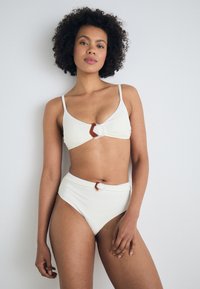 White textured bikini set featuring a triangular bralette with a brown accent buckle and high-waisted bottoms with matching details.