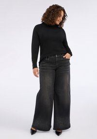 Suéter negro de cuello alto con acentos de botones en los puños, combinado con jeans de mezclilla negros de pierna ancha que presentan un efecto de degradado.
