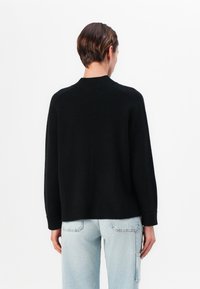 Svart strikkegenser med ribbestrikket rund hals, drop shoulder-design og lange ermer, kombinert med lyseblå denimbukser med baklommer.