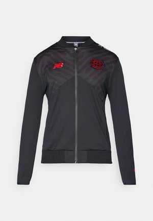 Sort jakke med lynlås foran, strukturerede øverste sektioner i mørkegrå med røde detaljer. Har ribbede manchetter og talje. New Balance-logoet er vist.