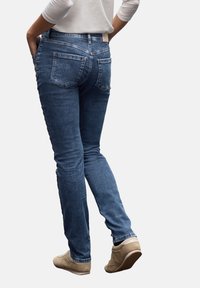 Vaqueros ajustados de mezclilla azul con una cintura de altura media, diseño de cinco bolsillos y detalles de costura. Llevados con calzado en tono beige claro.