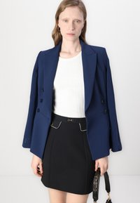 Marineblå dobbeltradet blazer med skræddersyet design, klapkraver og knapdetaljer, sættet med en hvid ribbet top og sort kort nederdel.