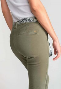 Olijfgroene broek met een aansluitend ontwerp, voorzien van een gemusterde tailleband en achterzakken. De stof lijkt glad met een lichte glans.