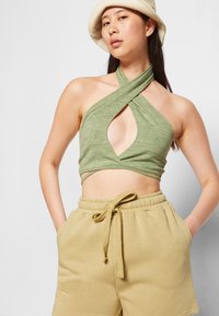 Top cropped verde com alças, de corte assimétrico e tecido texturizado, combinado com calções beges com cordão.