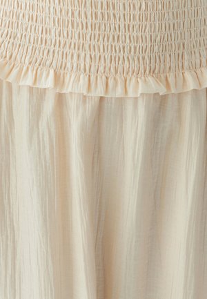 Gaiši bež kleita ar drapētu krūšu daļu, kam ir pūkaina apdare un plūstoša, teksturēta svārku daļa. Audums izskatās viegls un nedaudz krunkains.