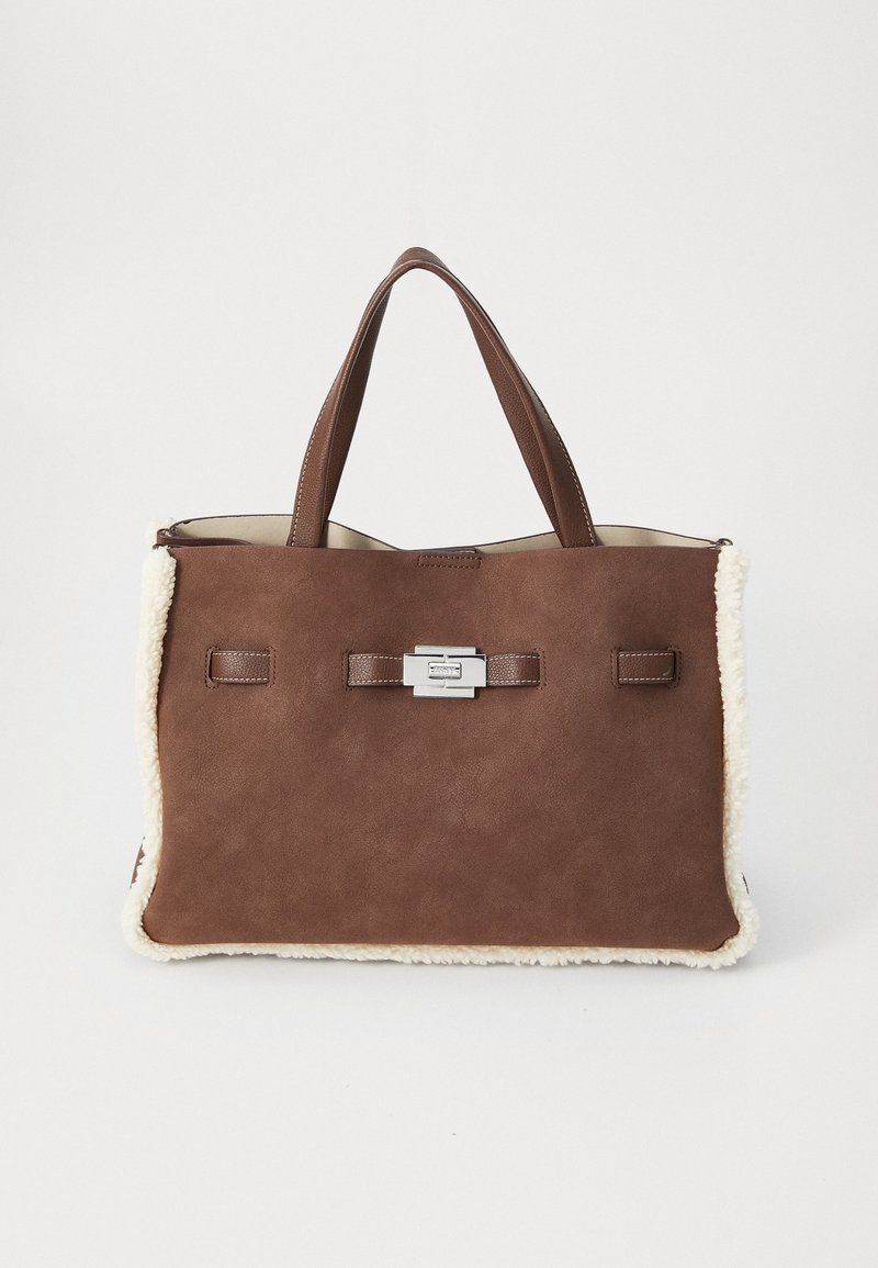 Sac fourre-tout en suède marron avec des bordures en fausse fourrure crème douce, doubles poignées et un fermoir rectangulaire en argent sur fond blanc uni.