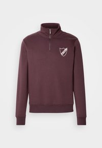 Sweat-shirt bordeaux à fermeture quart de zip, poignets et ourlet côtelés, avec un petit logo bouclier blanc sur la poitrine gauche.