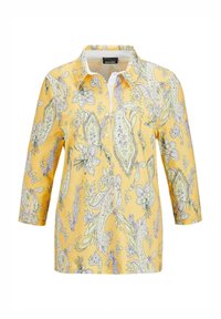 Geel shirt met kraag en driekwartmouwen, versierd met een paisley- en bloemenpatroon in paarse en groene tinten. Zachte stof textuur.