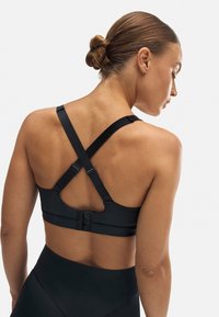 Sujetador deportivo negro con tirantes cruzados ajustables y cierre de gancho. Fabricado con una tela suave y con costuras mínimas para mayor comodidad.