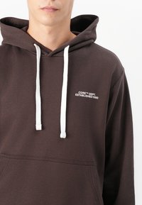 Brown hoodie with white drawstrings, ribbed cuffs, and a front pocket. The chest displays "CORE™ DEPT. ESTABLISHED 1990" in white.
