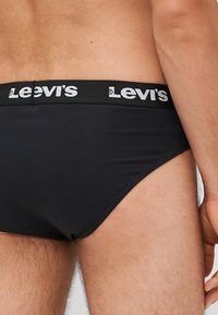 Bóxer negro de Levi's con cintura elástica que presenta el logo en blanco. Textura suave y diseño ajustado, que resalta las aberturas de las piernas y la parte trasera.