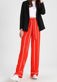Rood gestreepte wijde broek met hoge taille en strikceintuur, gecombineerd met een witte t-shirt en een zwart blazeren. Witte sneakers maken de outfit af.