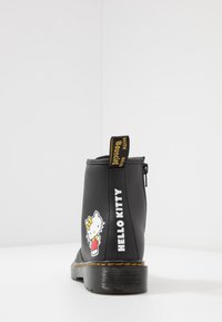 Černé kotníkové boty s žlutě šitým podpatkem, zadním zipem, poutkem, postavou Hello Kitty a textem "HELLO KITTY" na patě.