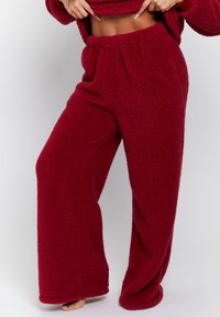 Burgundy fleecbyxor med en avslappnad passform, elastiskt midjeband och en mjuk, texturerad yta; bred bendesign som sträcker sig ner till golvet.
