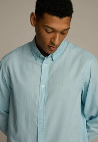 Jasnoniebieska koszula zapinana z przodu, wykonana z miękkiego, teksturowanego materiału, z kołnierzykiem, posiadająca pełny przód z listwą i guziki przypominające perły.