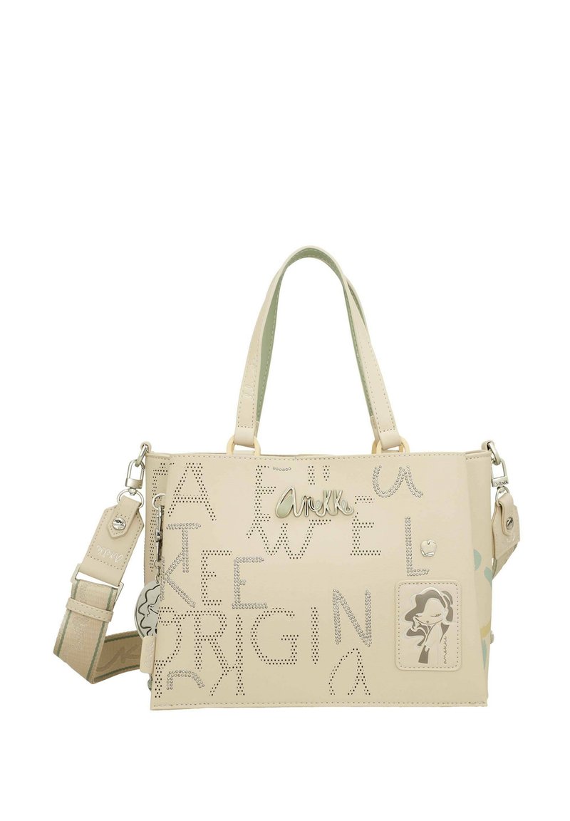 Bolso de mano de cuero beige con texto y diseño perforados. Cuenta con asas dobles, una correa desmontable y un acento decorativo en la silueta.