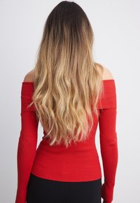 Haut rouge à côtes, épaules dénudées avec manches longues, coupe ajustée et tissu texturé. Fini lisse avec une couleur unie, sans motifs ni accents.