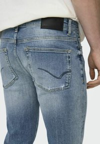 Heren blauwe denim jeans met een taps toelopende pasvorm, vervaagde textuur, twee achterzakken en een zwart leren label met merknaam op de tailleband.