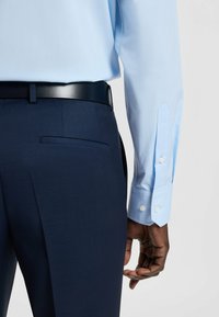 Camicia azzurro chiaro con polsini abbottonati, abbinata a pantaloni navy e una cintura in pelle nera, che mette in evidenza una vestibilità su misura e un design pulito.