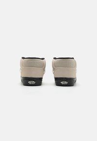 Beige semskede høysålede sneakers med svarte detaljer, polstret krage, gummisåle og preget "VANS"-logo på hælen.