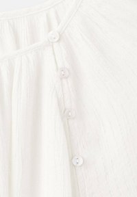 Weißer, strukturierter Stoff mit vertikalen Streifen, versehen mit fünf runden, transparenten Knöpfen entlang des Halsausschnitts zum Verschließen.