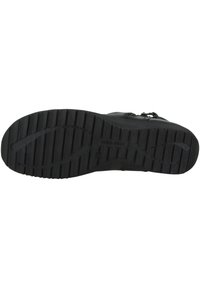 Schwarze Schuhsohle aus strukturiertem Gummi mit tiefen Profilen für besseren Halt, flachem Design und geprägten Branding-Details auf der Unterseite.