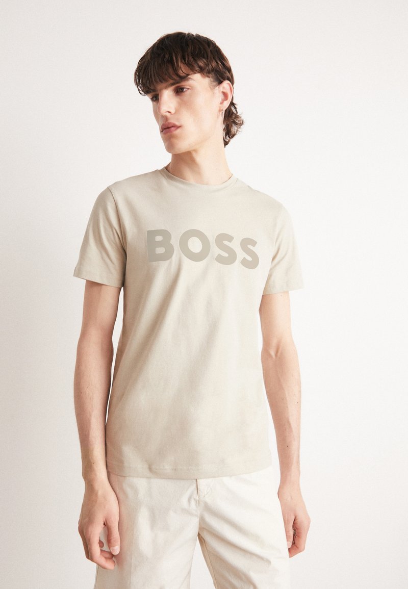 Beige, rövid ujjú póló, pamutból készült, elülső részén feltűnő szürke "BOSS" logóval, kerek nyakkivágással és laza szabással.