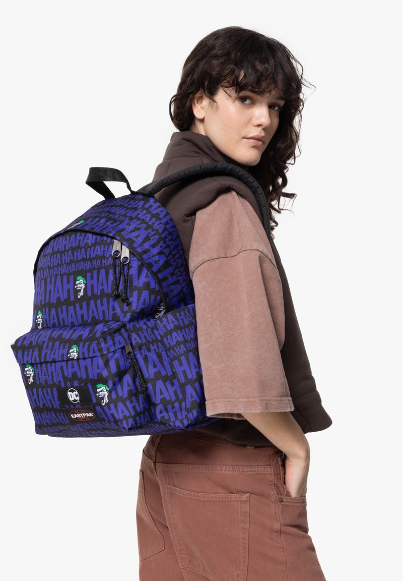 Mochila azul con patrón de "HA", que cuenta con un bolsillo frontal, tirantes ajustables y detalles bordados. Lleva al hombro.