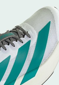 Scarpa da corsa grigia con accenti teal, dotata di una tomaia in mesh texturizzato, lacci piatti e una suola bianca ammortizzata. Contrassegnata "adizero."