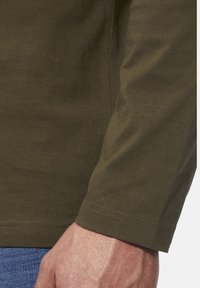 Olivgrünes Langarmshirt aus Baumwolle mit glatter Textur und geradem Schnitt am Ärmel. Sichtbare Nahtdetails entlang des Randes.