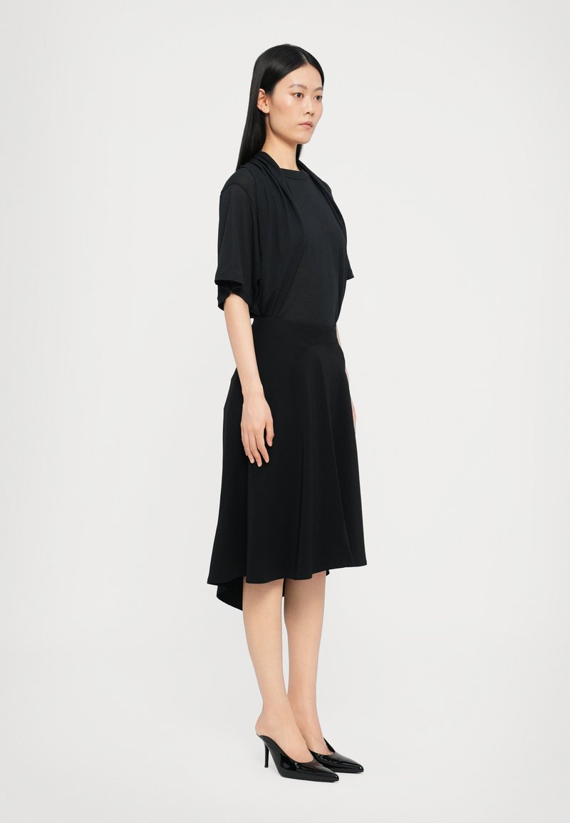Black dress with an asymmetrical hem, made of smooth fabric. Paired with black high-heeled shoes, featuring a pointed toe design.